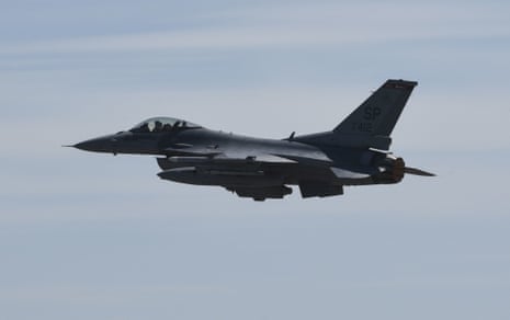 An F-16 fighter jet flies against a hazy sky, seen from the side