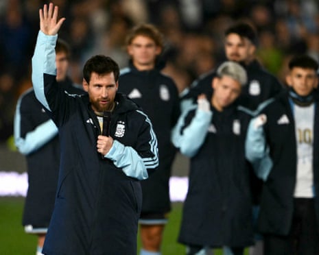 Lionel Messi holds a microphone and raises his hand while speaking to the crowd