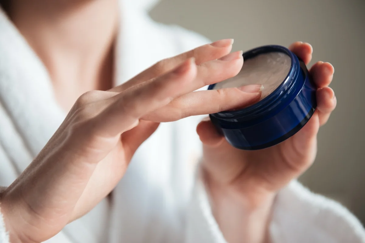 Close-up de uma jovem mulher mãos segurando um pote de creme ou pomada capilar. Metrópoles