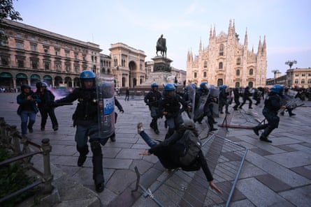 A protester falls backwards on to the ground as police with shields rush through a square