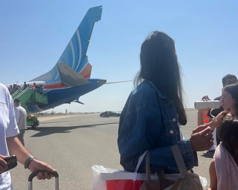 Passengers stand on the tarmac near a flydubai plane with visible tail damage