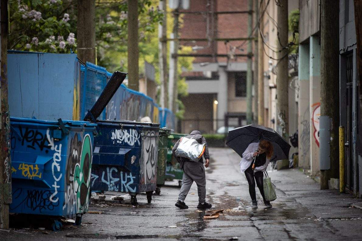 FILE - A woman prepares to smoke a cigarette in an alley after using illicit drugs at an outdoor supervised consumption site in the Downtown Eastside of Vancouver, on Thursday, May 27, 2021.